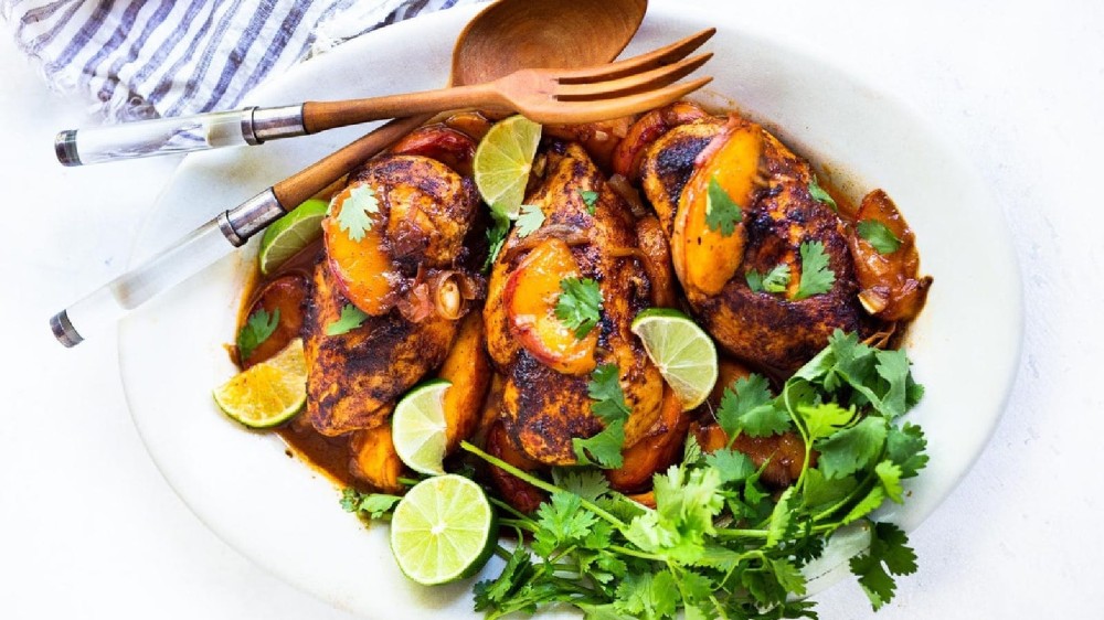 An oval serving plate filled with seared chili lime chicken topped with a warm peach glaze, fresh cilantro and lime wedges.