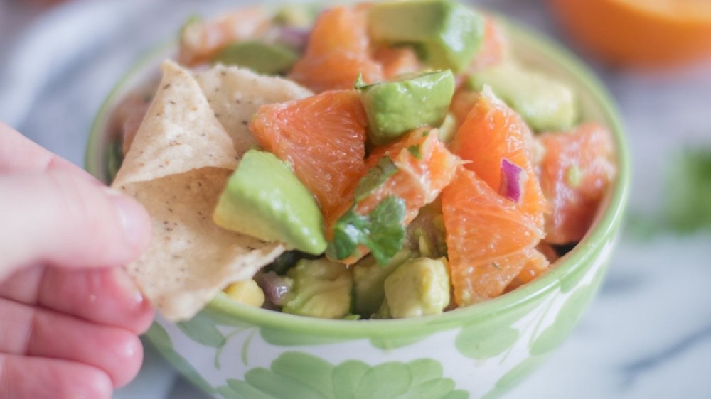 Someone dipping a chip in a bowl of orange and avocado salsa. 